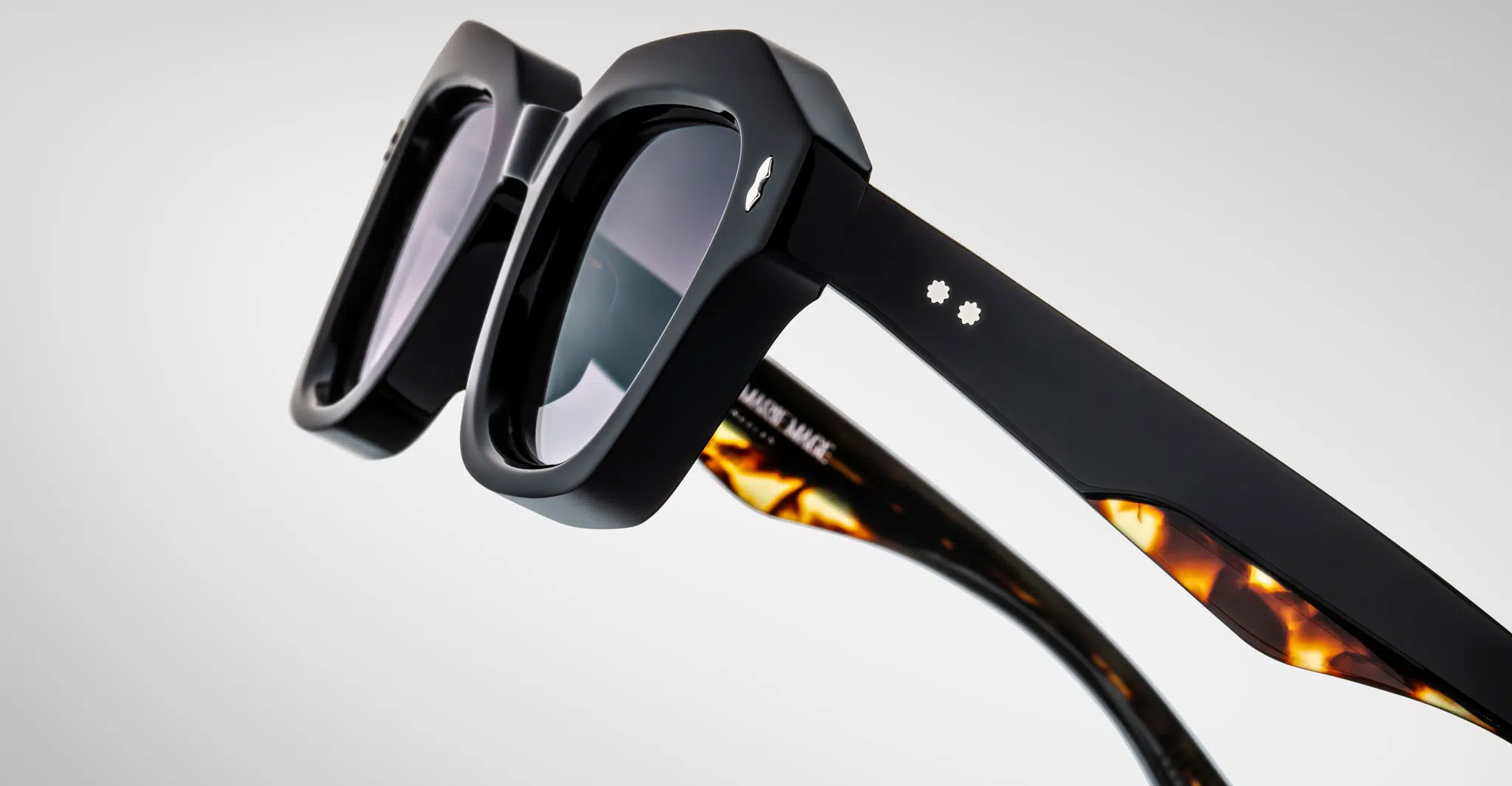 Detailed profile view of a pair of Jacques Marie Mage Eichler black, thick-framed sunglasses with grey lenses on a plain background