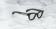 The Jacques Marie Mage Julien sunglasses, featuring thick black frames, green-tinted lenses, and silver-detailed temples with inner branding, rest on a white marble surface.