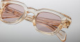 Close-up of Jacques Marie Mage Julien transparent beige rectangular eyeglasses with light brown tinted lenses and detailed engravings on the temples, set against a light gray background.
