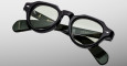 The Jacques Marie Mage Kellerman features black round eyeglasses with slightly tinted lenses, displayed on a light grey background. The temples showcase brand markings and gold lettering details.