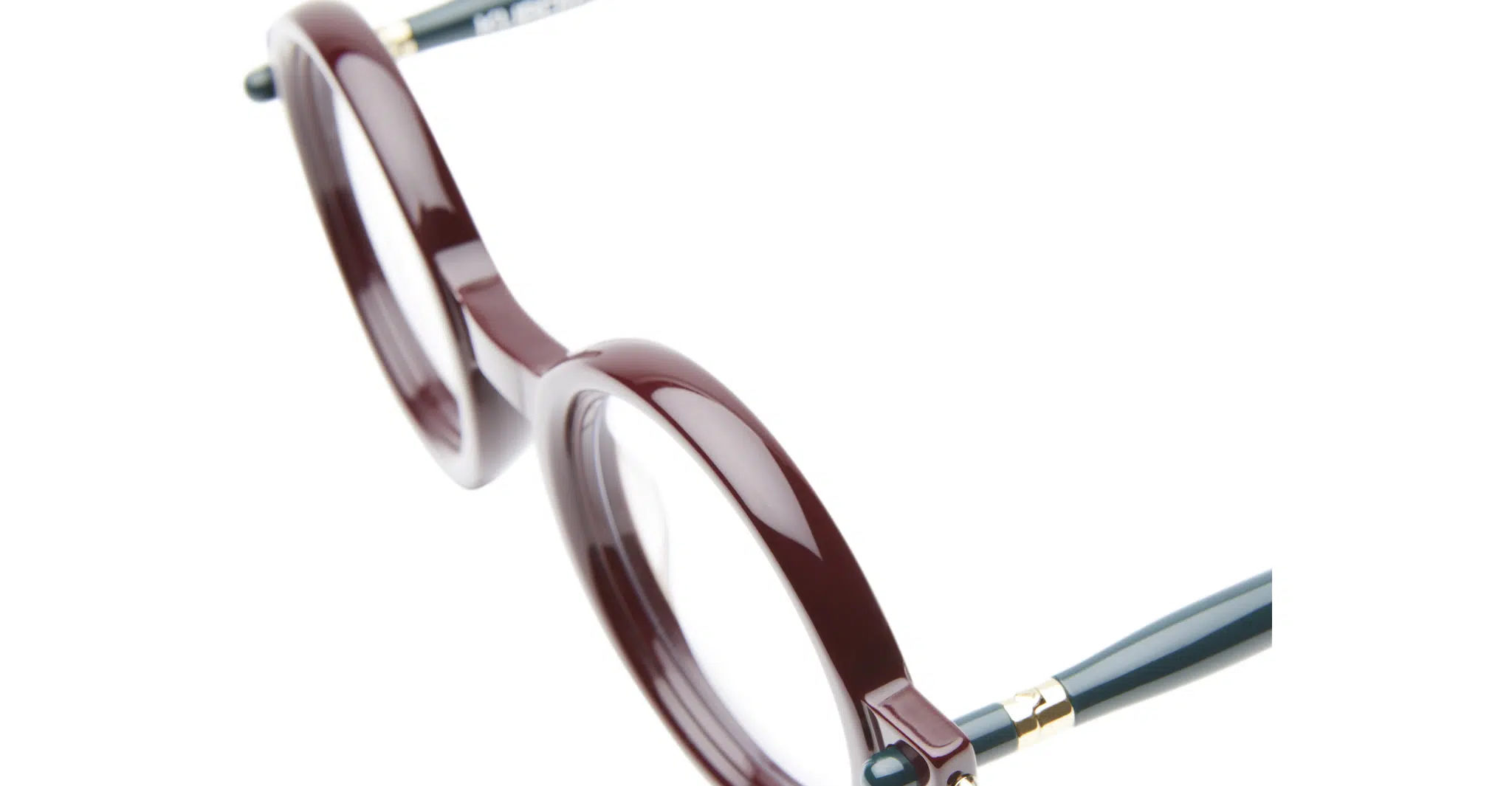 Kuboraum-P1-Bordeaux-KRO0P1DR000000OP-Detail3-Dan-Deutsch A close-up of Kuboraum P1 eyeglasses featuring round, thick burgundy rims and dark green arms, set against a white background.