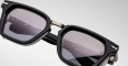Close-up of Jacques Marie Mage Borodino sunglasses, featuring a black rectangular frame, metal hinges, and dark tinted lenses. Small white markings and Japanese text appear on the inside of the left temple arm.