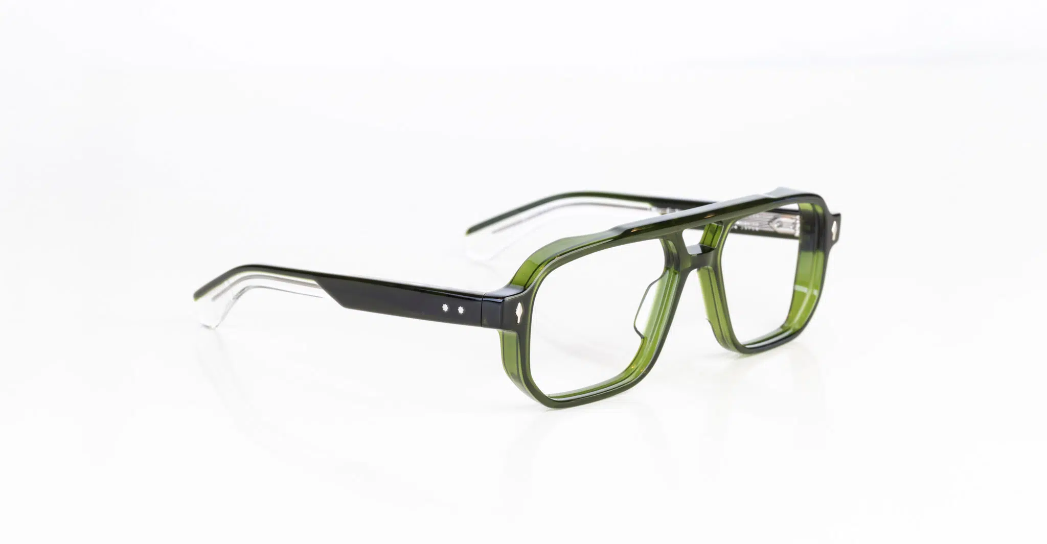 A pair of Jacques Marie Mage Evans rectangular eyeglasses with thick, translucent green frames and black arms rests on a white surface. The temples feature two small silver dots near the hinges.