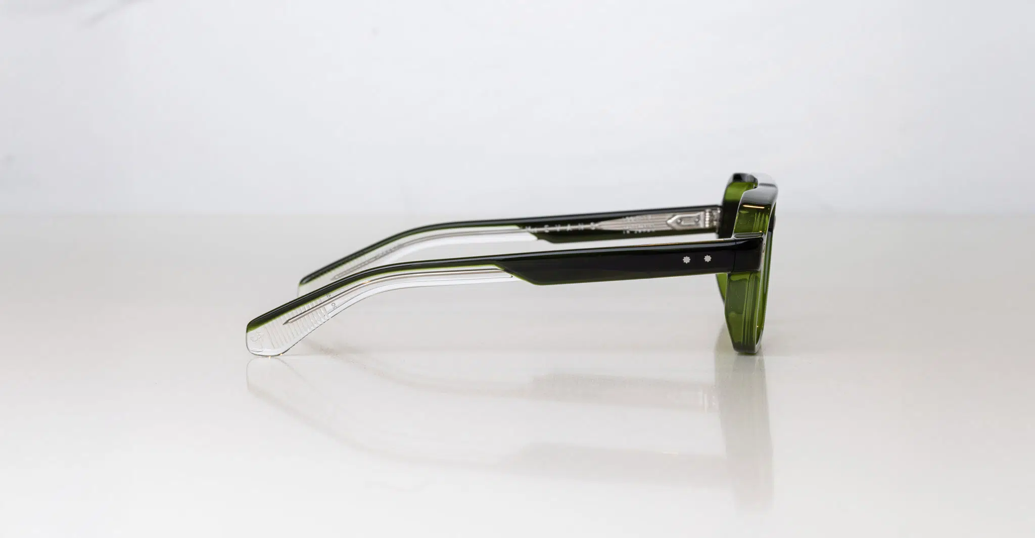 The Jacques Marie Mage Evans eyeglasses, featuring green frames and transparent temples, are displayed on a white surface and viewed from the side.