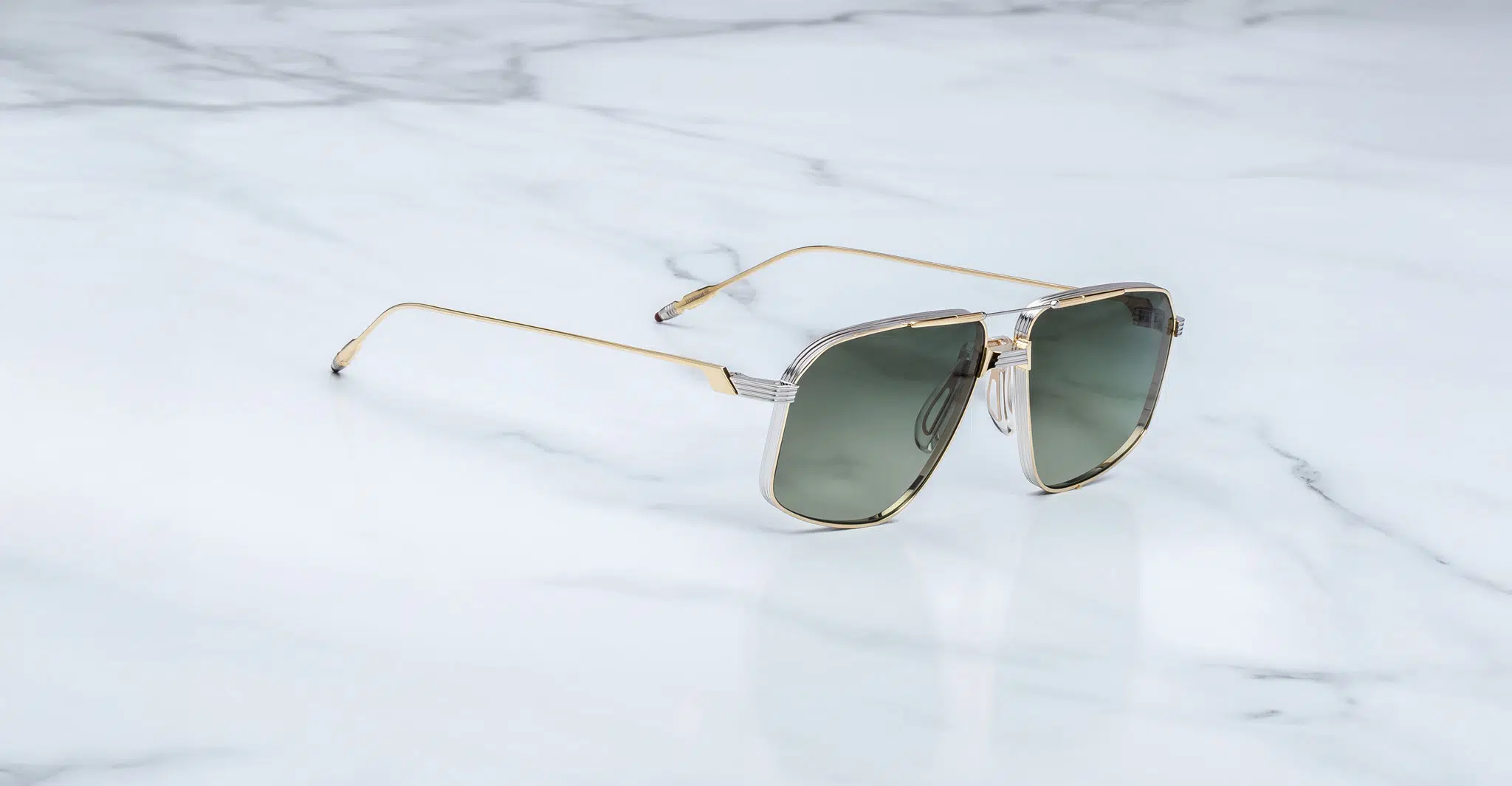 Jacques-Marie-Mage-Jagger-Musket-JMMJG-12M-Profile-Dan-Deutsch The Jacques Marie Mage Jagger sunglasses feature green-tinted lenses and gold metal frames, elegantly displayed on a white marble surface.