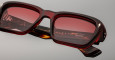 Close-up of rectangular red Jacques Marie Mage Walker sunglasses with tinted lenses, showing the inside of one arm etched with “HANDCRAFTED IN SPAIN.” The glossy frame highlights the premium craftsmanship.