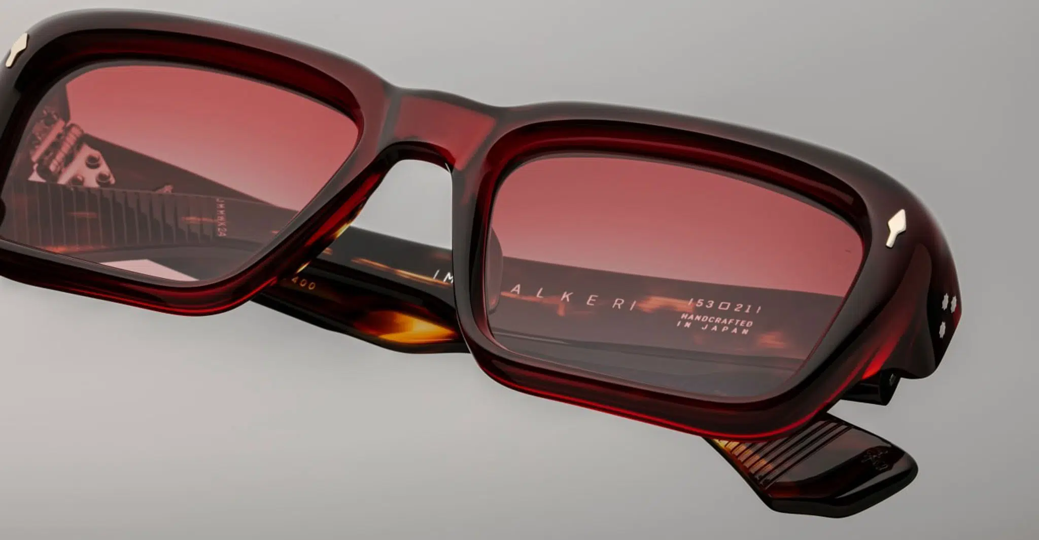 Close-up of rectangular red Jacques Marie Mage Walker sunglasses with tinted lenses, showing the inside of one arm etched with “HANDCRAFTED IN SPAIN.” The glossy frame highlights the premium craftsmanship.