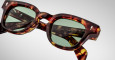 Close-up of Jacques Marie Mage Julien tortoiseshell sunglasses with green-tinted lenses, highlighting the frames detailed texture and visible inner-arm branding, set against a plain light background.