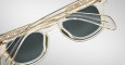 Close-up of Jacques Marie Mage Julien transparent sunglasses with gold accents and dark lenses, highlighting the intricate patterns on the frames and temples against a light gray background.