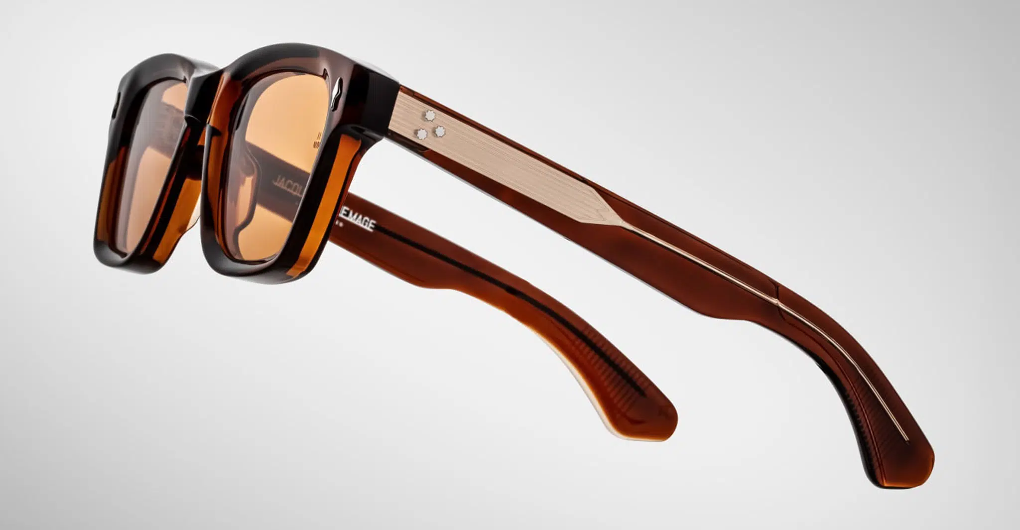 The Jacques Marie Mage Sonata is a pair of brown, rectangular sunglasses with thick frames and temples, metallic accents, and small round rivets near the hinges, displayed against a light gray background.