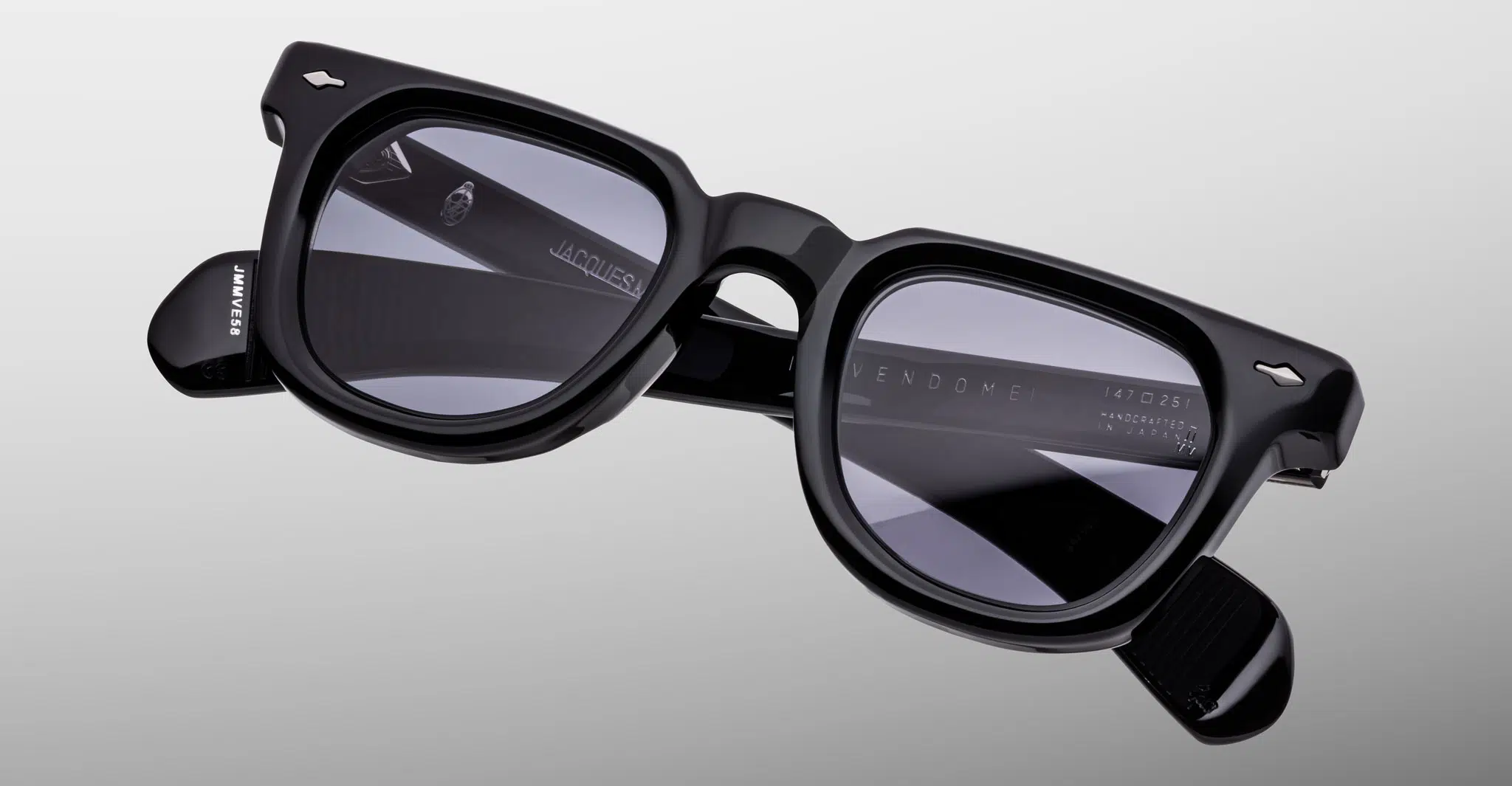 A pair of Jacques Marie Mage Vendome black rectangular sunglasses with thick frames and dark tinted lenses is displayed on a light gray background, with brand and model details visible on the inner temples.