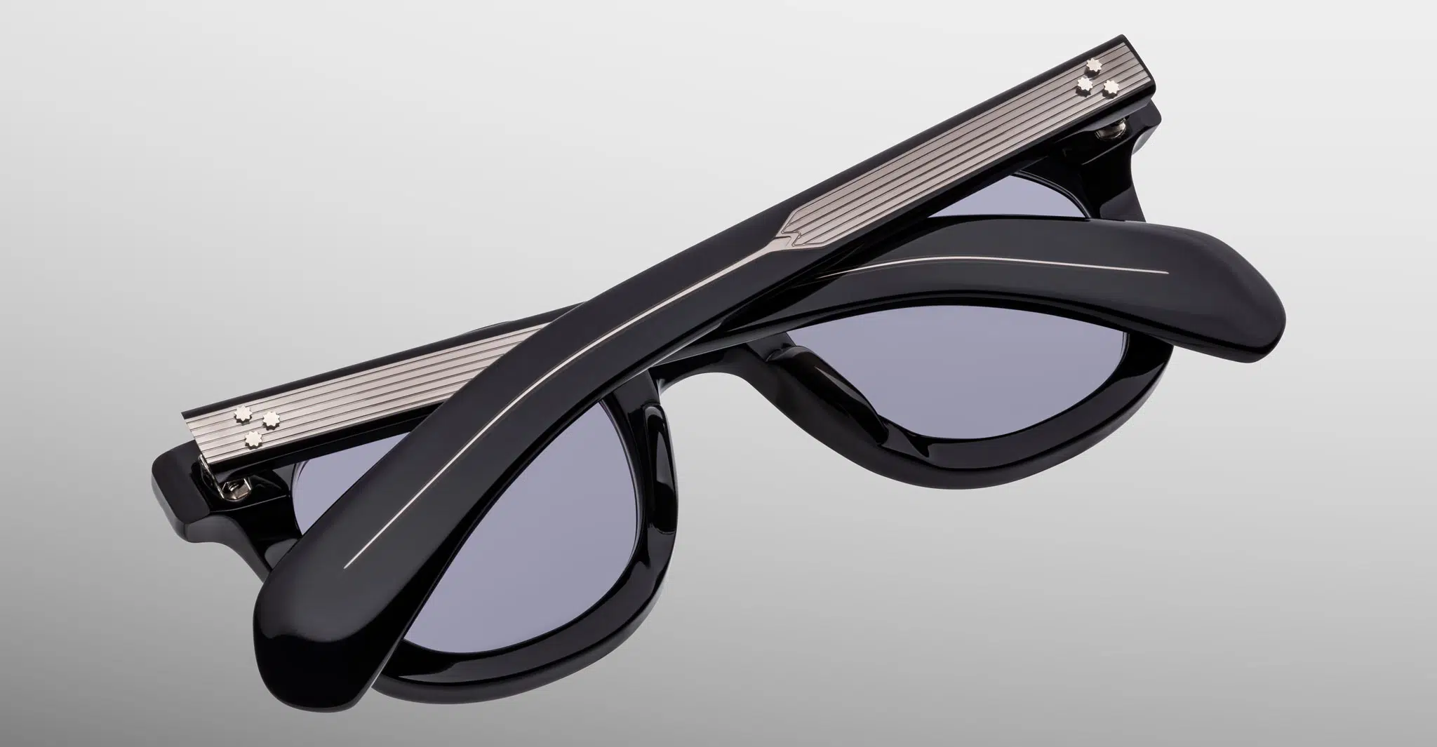 The Jacques Marie Mage Vendome sunglasses, featuring black frames with metallic accents and dark tinted lenses, are displayed folded shut with crossed arms on a light gradient background.