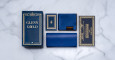A flat lay of blue and gold Jacques Marie Mage Glenn Gould packaging on a marble surface, with a large box labeled Glenn Gould, a booklet, a cleaning cloth, a case and a certificate