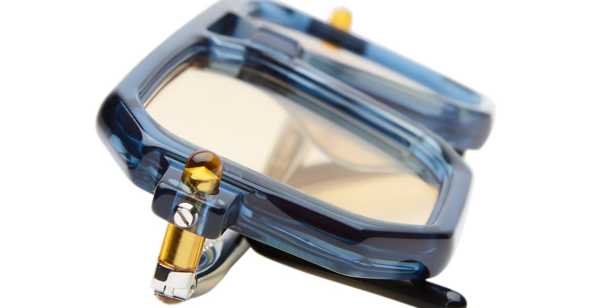 Kuboraum-P8-BBY-Biscay-Blue-KRS0P8BBY000002R-Detail1-Dan-Deutsch Close-up of Kuboraum P8: modern blue sunglasses with thick, translucent frames and yellow-tinted lenses, shown at an angle to highlight their geometric design and metal hinge detail.