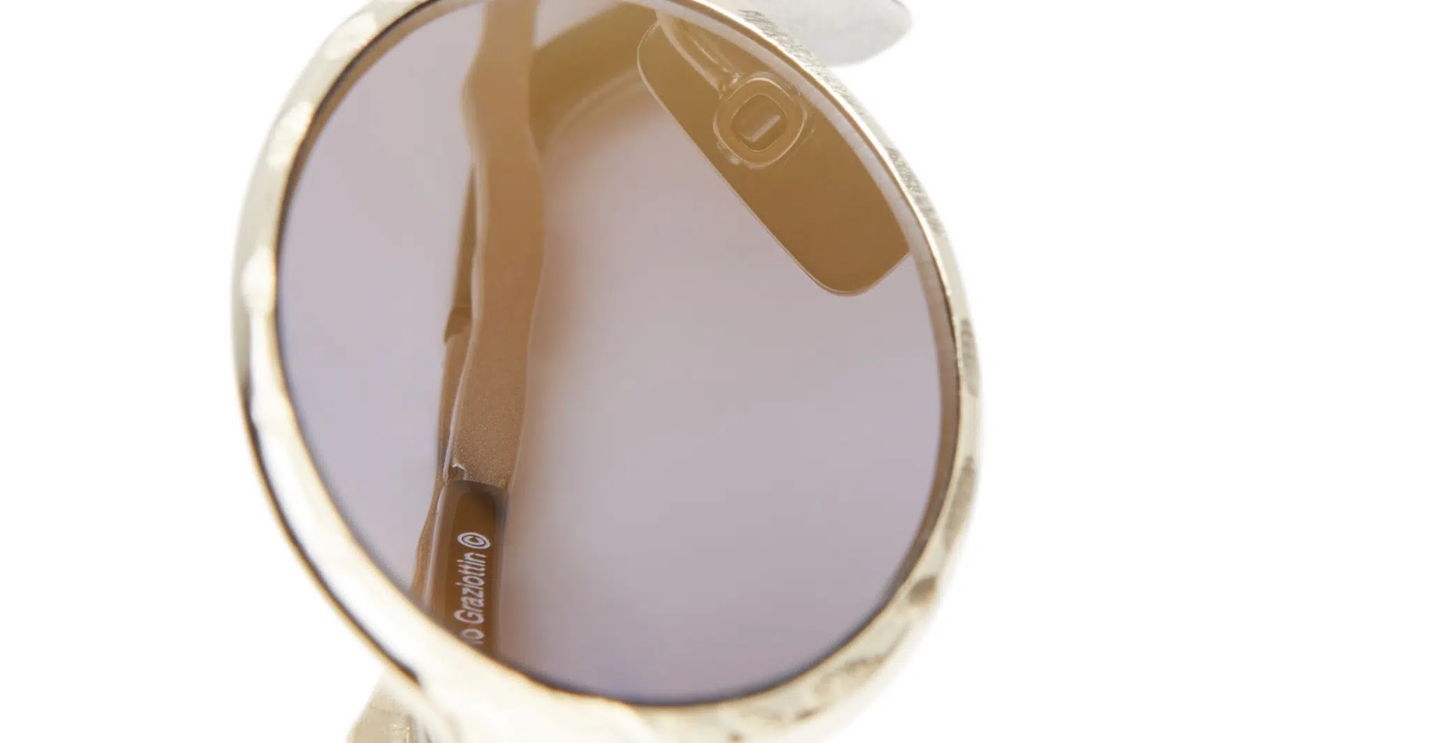 Kuboraum-Z24-GG-Gold-KRSZ24GG000000GF-Detail3-Dan-Deutsch Close-up of Kuboraum Z24 round sunglasses with gold frames and brown-tinted lenses, showing the inner side of one arm against a white background. The brand name appears faintly on the arm.