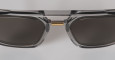 Close-up of Masunaga Master of Craft - 002: dark rectangular sunglasses featuring a metallic frame with a gold accent on the nose bridge, displayed against a light gray background.