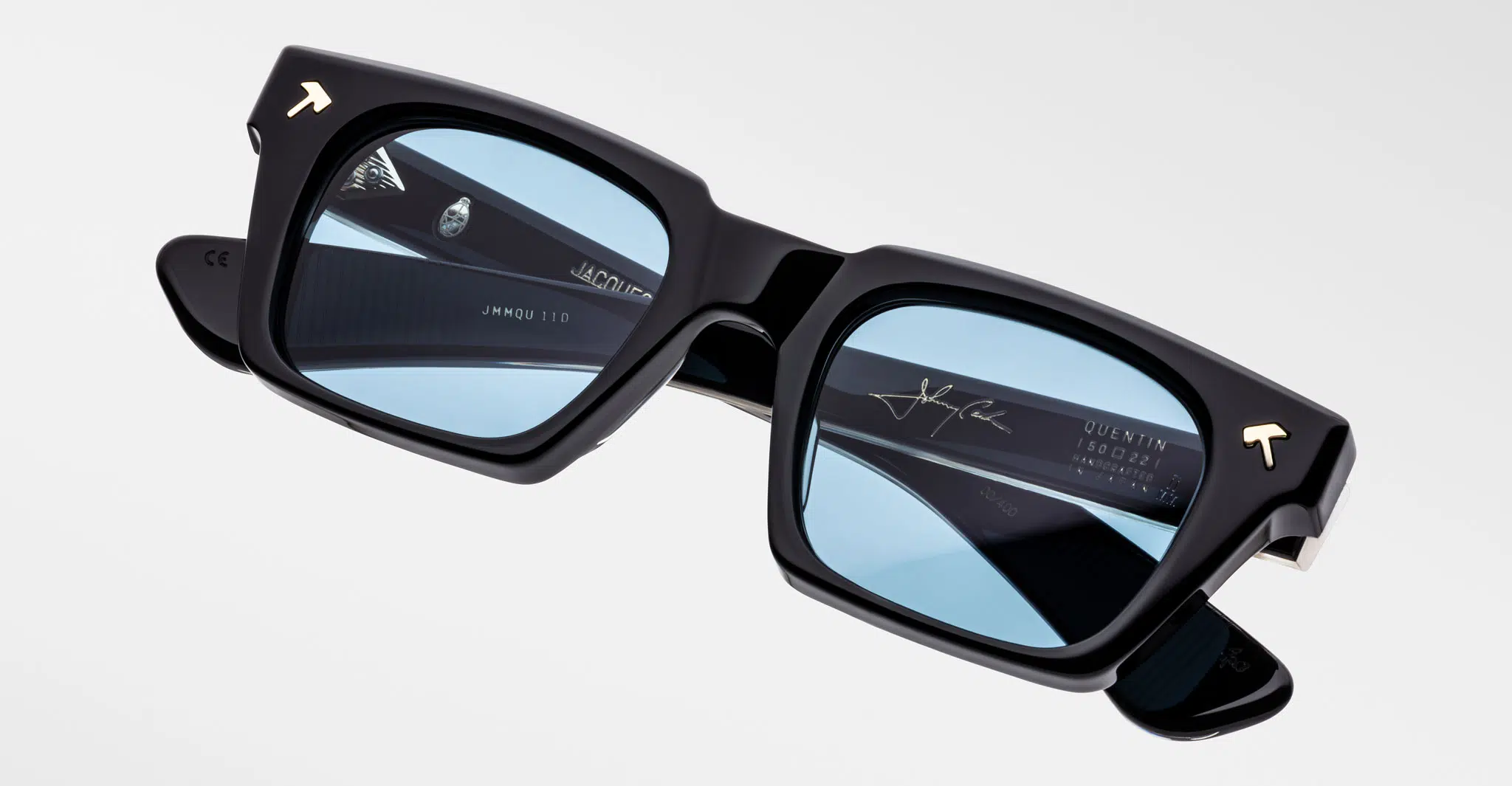 The Jacques Marie Mage Quentin eyeglasses are black and rectangular with light blue tinted lenses, silver detailing, and a signature on the inside of one arm.