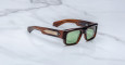 Jacques Marie Mage Donat rectangular sunglasses with thick brown tortoiseshell frames, green lenses, and metallic temple accents, shown on a white marble surface.
