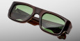 The Jacques Marie Mage Donat sunglasses feature thick, dark brown rectangular frames and green-tinted lenses, shown against a light gray background. Branding is visible on the inner temples.