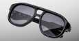 The Jacques Marie Mage Jasper sunglasses feature an oversized black frame with dark tinted lenses, a bold thick design, and a double bridge, displayed on a gradient gray background.