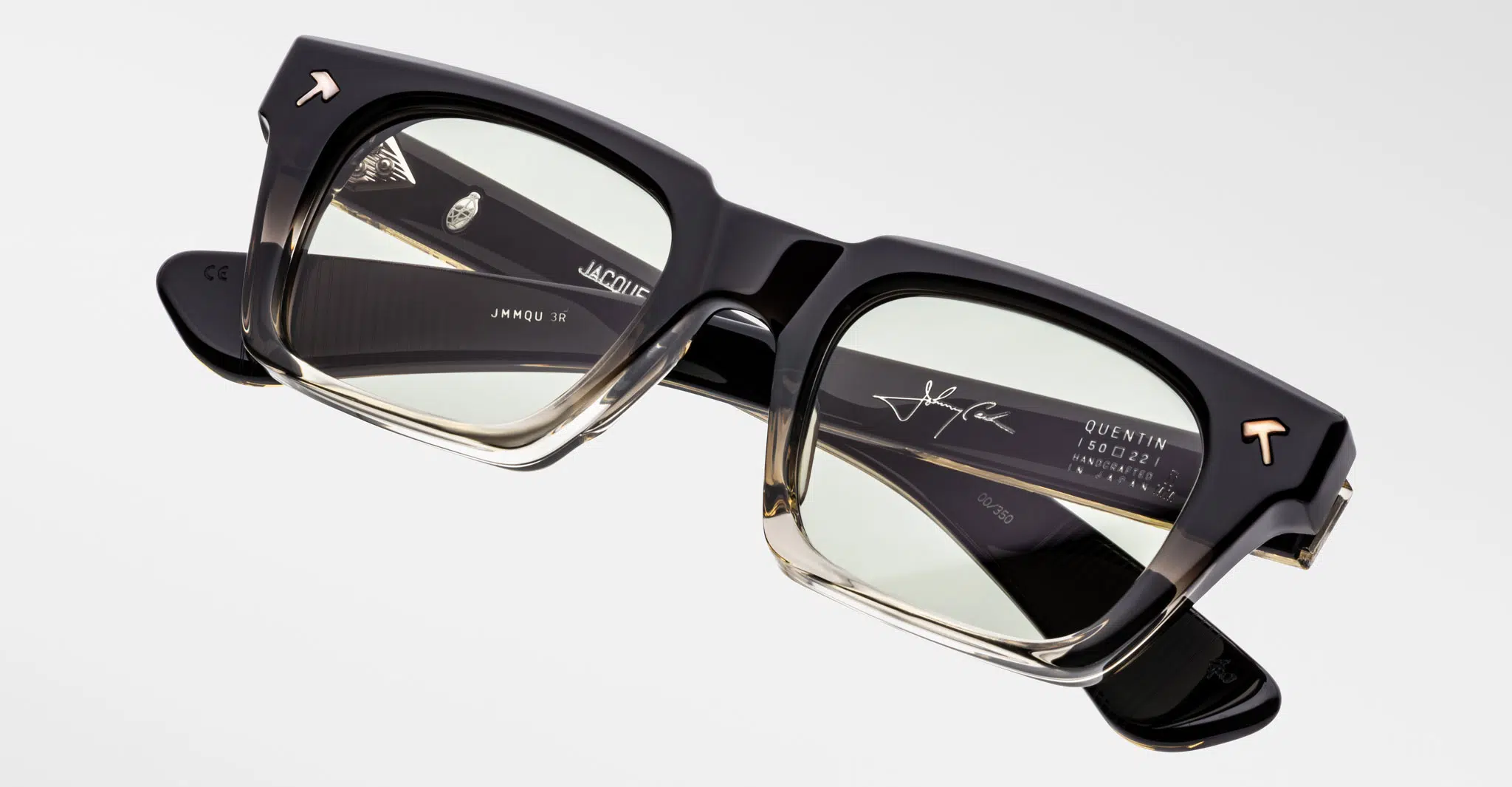 The Jacques Marie Mage Quentin eyeglasses feature rectangular, thick black-to-clear gradient frames, visible metal hinges, and light yellow lenses. Custom details and a signature adorn the arms. Displayed on a white background.