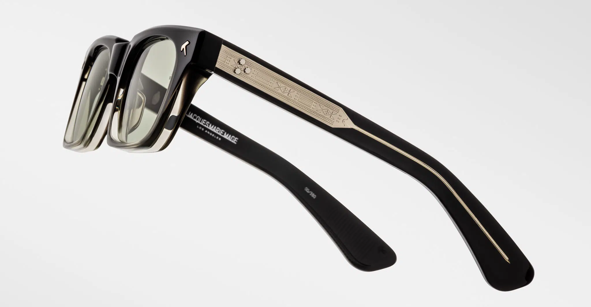 A pair of Jacques Marie Mage Quentin black sunglasses with rectangular frames, light tinted lenses, and gold detailing on the arms. MADELEINE & MARIE is labeled inside the arm. Set against a white background.