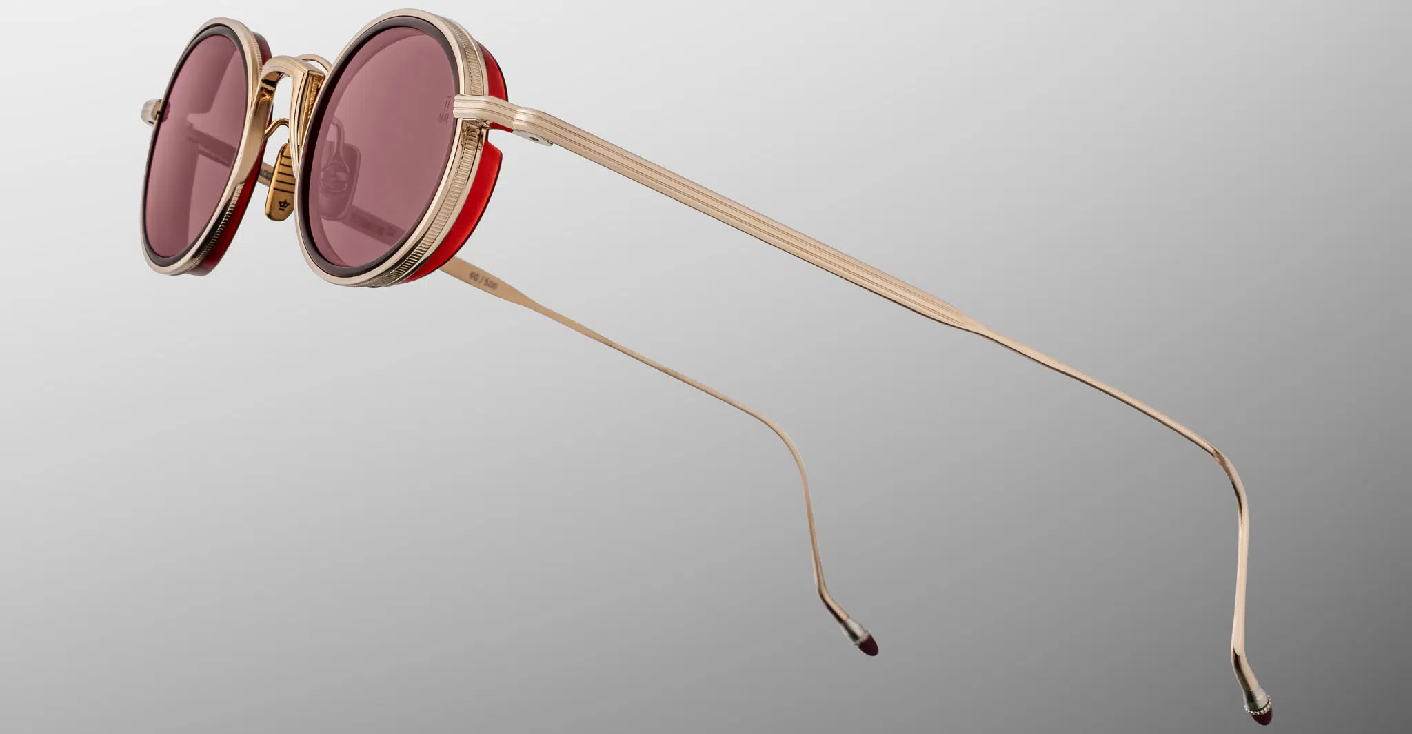The Jacques Marie Mage Varda round sunglasses feature gold metal frames, thin gold arms, and pink-tinted lenses, displayed against a gray gradient background.