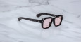 The Jacques Marie Mage Vivienne sunglasses feature a stylish black frame and pink-tinted lenses, elegantly displayed on a white marble surface.