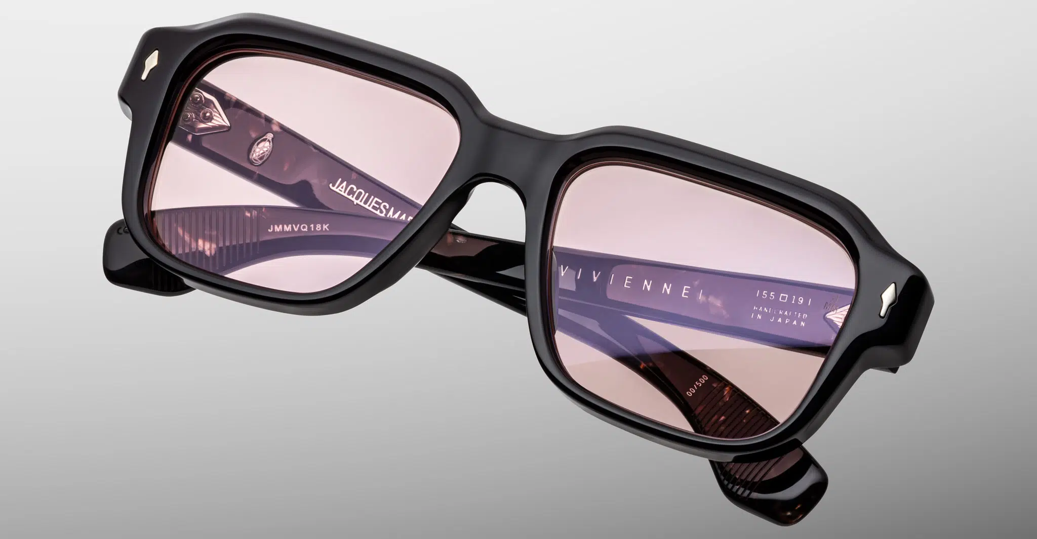 Black-framed square eyeglasses with light pink lenses are displayed on a gray background, featuring the Jacques Marie Mage Vivienne branding on the temple.
