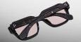The Jacques Marie Mage Vivienne sunglasses feature a stylish black frame with light pink lenses, marbled temples, and gold accents near the hinges. Shown folded from above on a plain gradient light gray background.