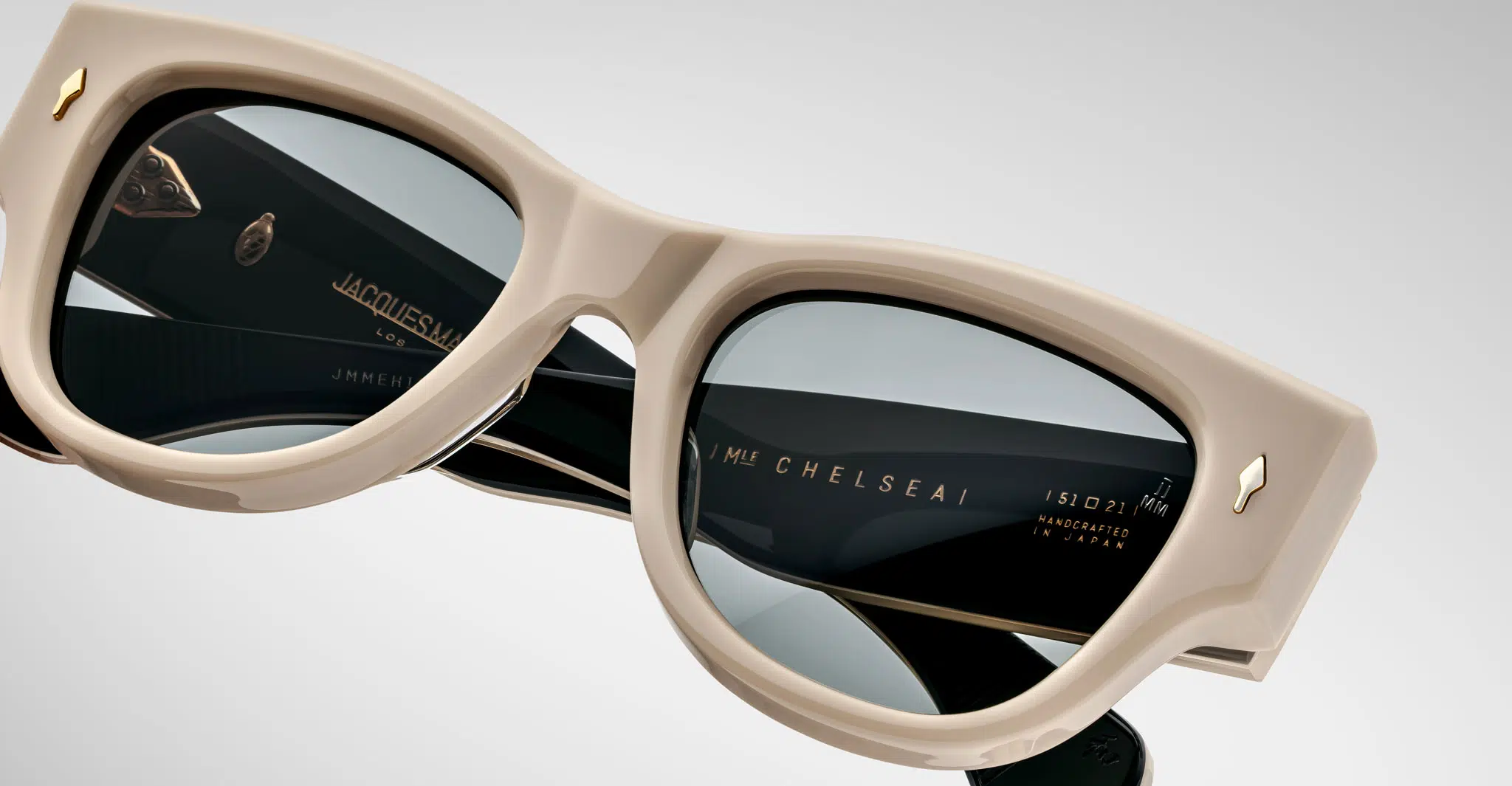 A close up view of a pair of Jacques Marie Mage Chelsea beige, thick-framed sunglasses with dark lenses