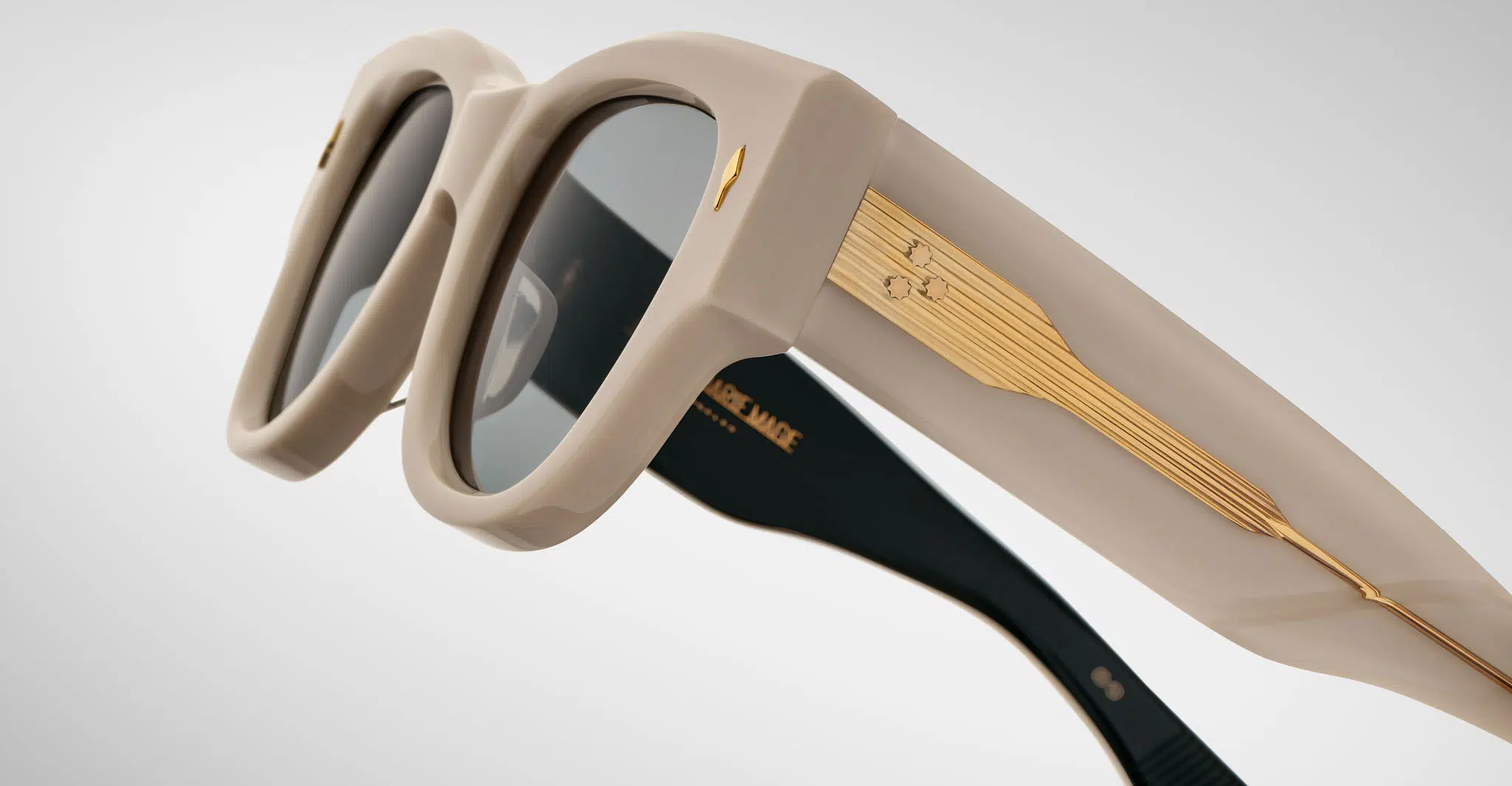 A close up profile view of a pair of Jacques Marie Mage Chelsea beige, thick-framed sunglasses with dark lenses