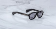 Jacques Marie Mage Richard black sunglasses with dark lenses and thick frames rest on a white marble surface, with the brand name visible on the inside of one temple arm.