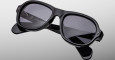 The Jacques Marie Mage Richard sunglasses feature thick, glossy black frames with dark lenses and visible brand markings on the arms, displayed against a light gray background.