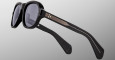 The Jacques Marie Mage Richard sunglasses feature thick black frames, dark lenses, and metallic gold accents with lined temples, displayed on a light gray background.