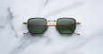 The Jacques Marie Mage Atkins are square-shaped sunglasses with gold frames and green lenses, displayed on a white marble surface.