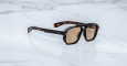 The Jacques Marie Mage Evans sunglasses, featuring thick dark tortoiseshell frames and brown-tinted lenses, rest on a white marble surface.
