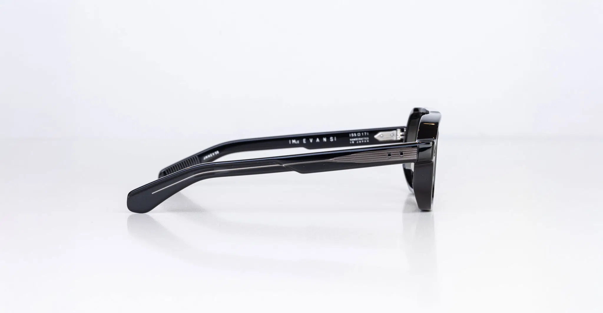 The Jacques Marie Mage Evans eyeglasses are black and rectangular, shown from the side on a white surface, with straight temples featuring subtle horizontal lines and silver detailing by the hinges.