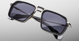 The Jacques Marie Mage GT-R features rectangular black frames, dark tinted lenses, and metallic accents on the bridge and temples, showcased against a neutral gradient background.