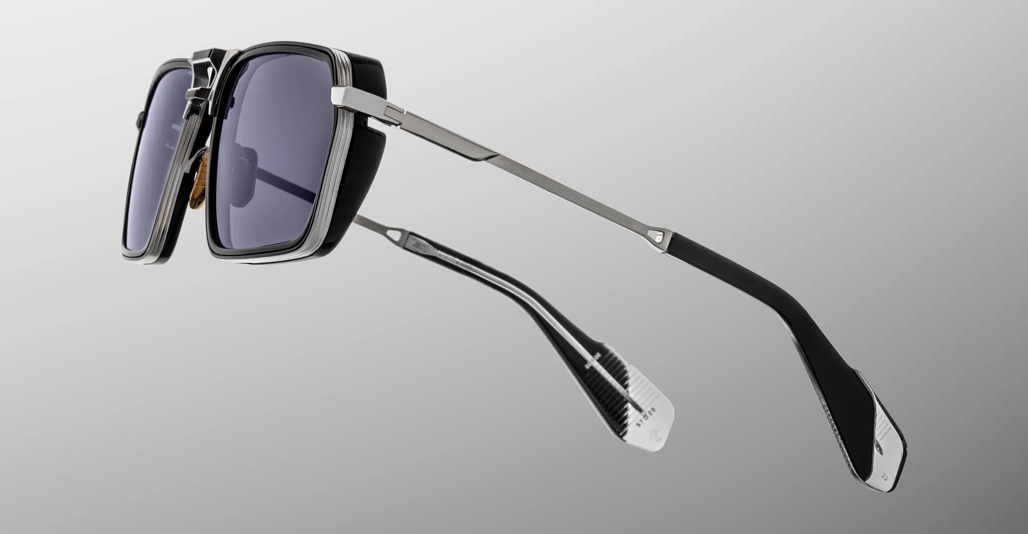 A pair of Jacques Marie Mage GT-R sunglasses featuring modern rectangular thick black frames, dark tinted lenses, and slim metallic arms, photographed against a plain grey gradient background.