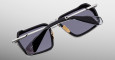 The Jacques Marie Mage GT-R sunglasses feature a black rectangular frame, silver metal arms, and dark tinted lenses, shown resting upside down on a neutral gradient background.