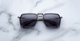 A pair of Jacques Marie Mage GT-R black square-framed sunglasses with dark lenses is displayed on a white marble surface.