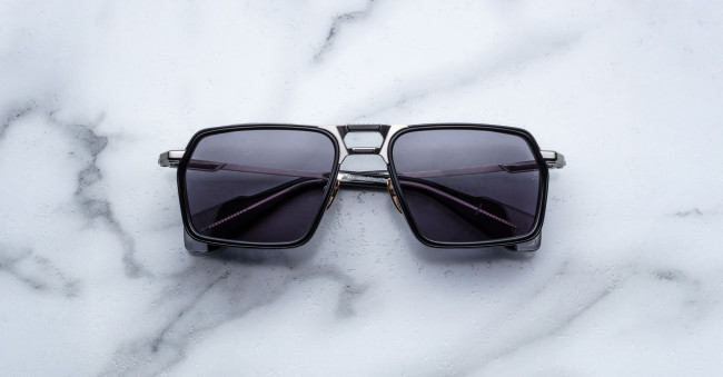 A pair of Jacques Marie Mage GT-R black square-framed sunglasses with dark lenses is displayed on a white marble surface.