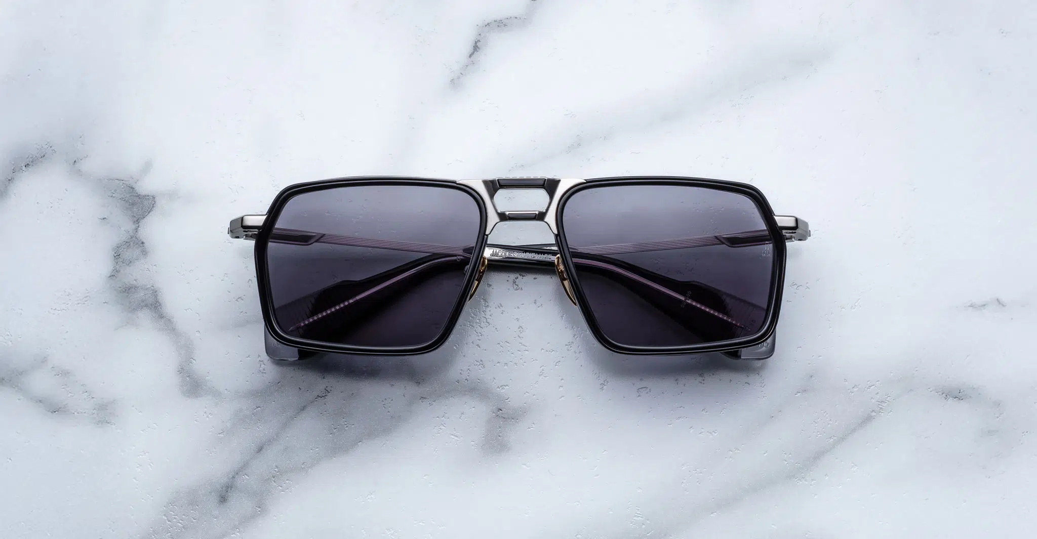 A pair of Jacques Marie Mage GT-R black square-framed sunglasses with dark lenses is displayed on a white marble surface.