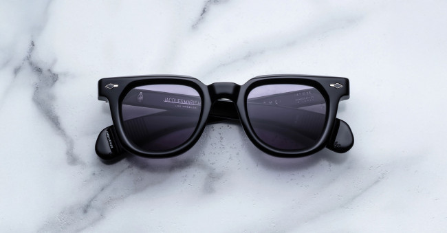 Jacques Marie Mage Vendome black cat-eye sunglasses with dark lenses and silver corner accents rest on a white marble surface with gray veining; the folded arms highlight the frame’s elegant details.