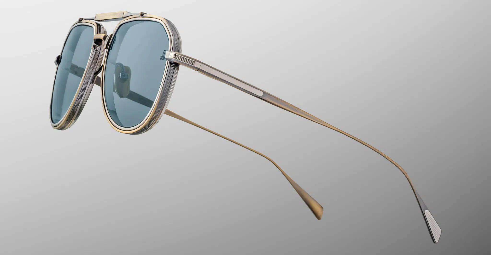 The Jacques Marie Mage Cougar sunglasses feature blue-tinted lenses, metallic frames, and long gold-colored arms, displayed against a plain light gray background.