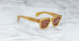 A pair of Jacques Marie Mage Fellini square sunglasses with amber frames and brown tinted lenses rests on a white marble surface.