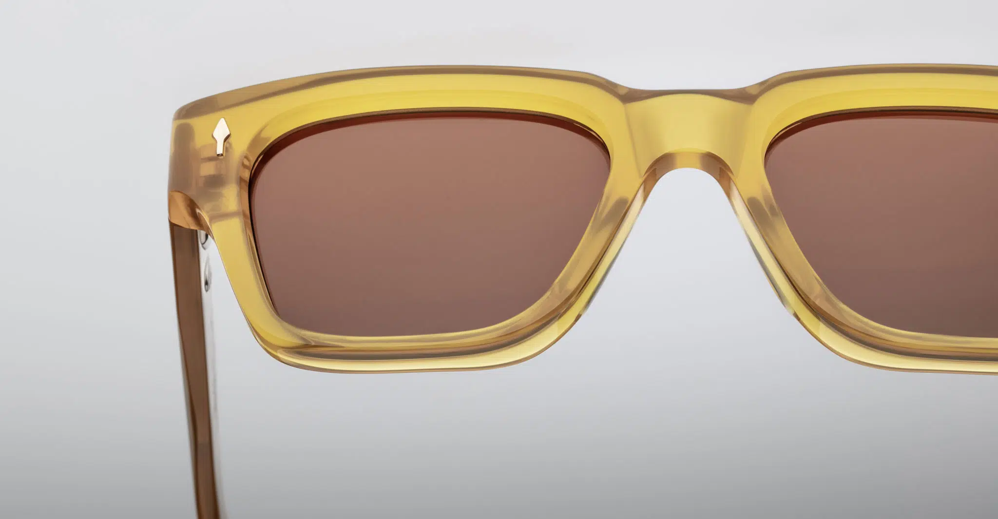 Close-up of Jacques Marie Mage Fellini rectangular sunglasses featuring translucent yellow frames and brown-tinted lenses set against a plain, light background.