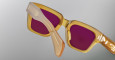 Close-up of Jacques Marie Mage Fellini sunglasses in yellow-orange with pink lenses, highlighting the detailed frame and hinge area against a light gray background.