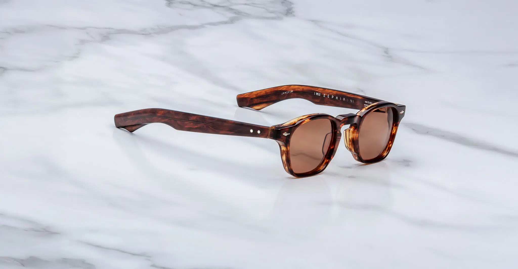 The Jacques Marie Mage Zephirin brown tortoiseshell sunglasses with round lenses rest on a white marble surface.
